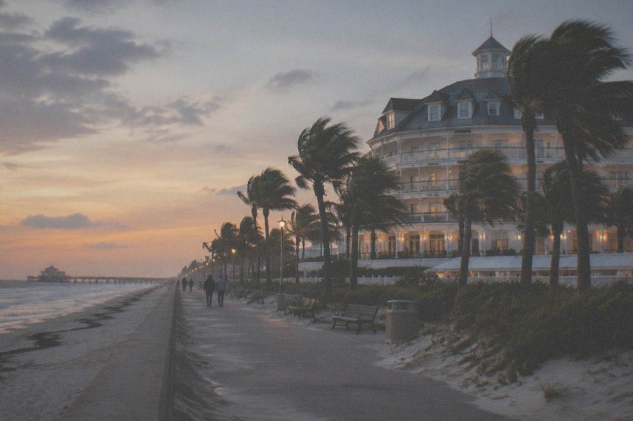 Historic beachfront hotel with palm trees along a seawall boulevard at dusk