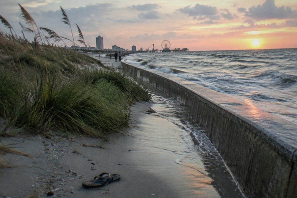 Long concrete seawall curving along the shoreline at dusk with waves against it