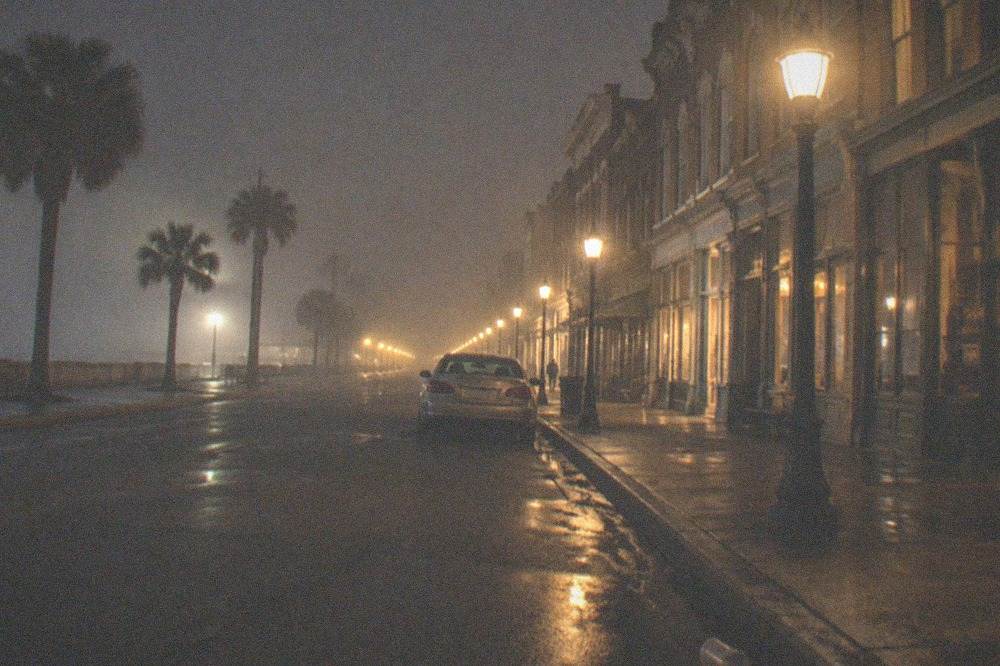 Empty downtown Galveston street at night with lit storefronts and a parked car along the curb