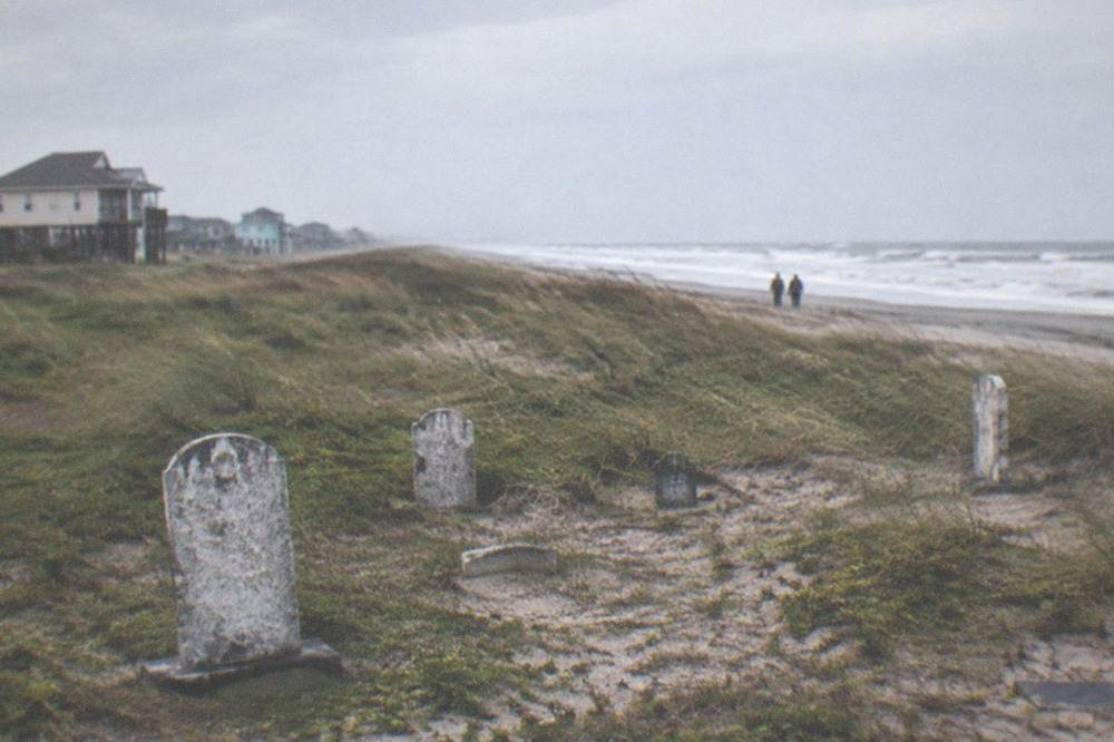 Sandy ground with scattered historic grave markers near the Galveston shoreline