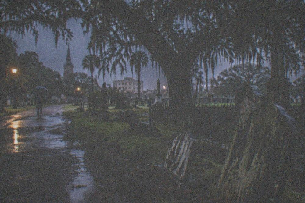 A gravel path through a dark cemetery with old trees and scattered headstones