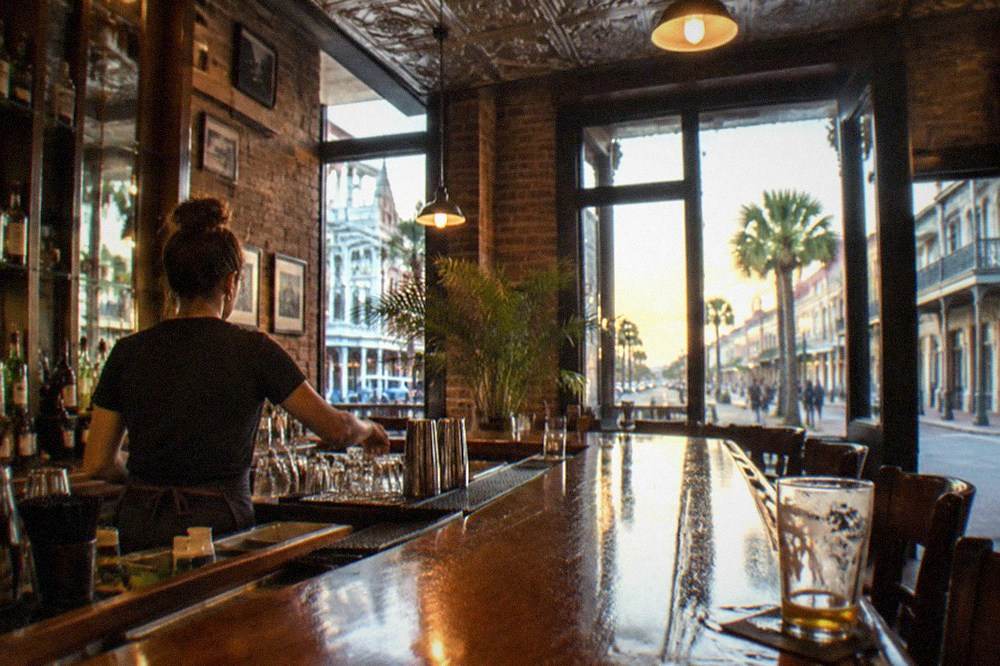 A bartender setting out glasses on a polished bar top in warm evening light